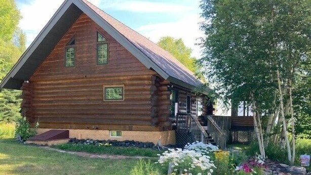 A log cabin with a steep gable roof, a front porch, and a stone foundation.