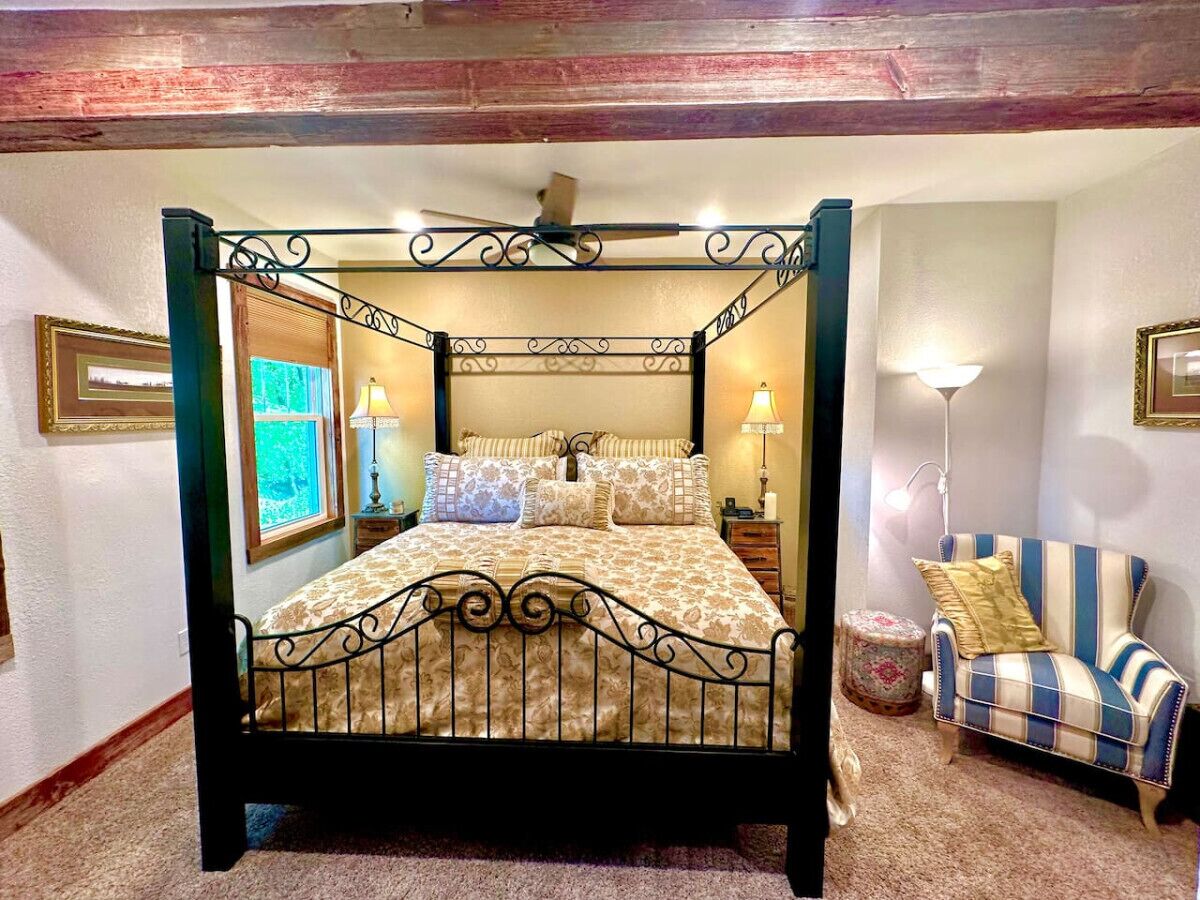 Una cama con dosel con una colcha estampada, una mesita de noche con una lámpara y un sillón a rayas.