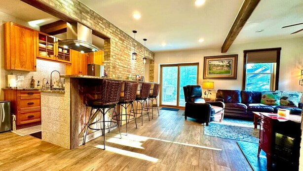 A spacious kitchen with a brick accent wall, wooden cabinets, and a bar area with stools. - Home Port Vacation Escape, Luxury Historic Home, Walk to Port, Beach, Shops (Port Washington)