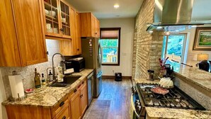 A modern kitchen with wooden cabinets, a stainless steel range hood, and a view of the outdoors through a window. - Home Port Vacation Escape, Luxury Historic Home, Walk to Port, Beach, Shops (Port Washington)