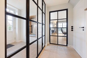 A hallway with a glass door leading to a room with a chair and a table. - Haus Süderjen - Charakter. Luxus. Reet. - Hsj/03 (Sylt)