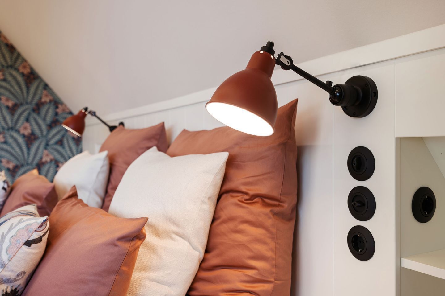 A bedroom with a bed, pillows, and a wall-mounted lamp.