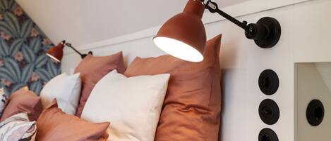 A bedroom with a bed, pillows, and a wall-mounted lamp.