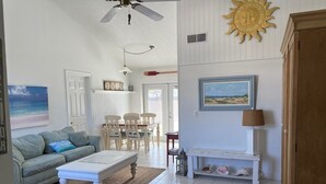 A spacious living room with a white ceiling fan, a dining area with wooden chairs, a white coffee table, and a painting of a beach scene. - Freshly remodeled, wonderfully located home in North Sarasota. (Sarasota)