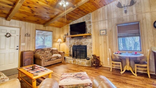 A cozy cabin interior with a stone fireplace, wooden walls, a ceiling fan, and a dining area. - Private - Spacious- Creek Lined Cabin  (Cosby)