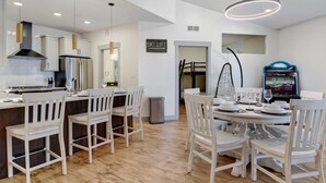 Una cucina moderna con mobili bianchi, un frigorifero in acciaio inossidabile e un'area pranzo con sedie bianche e un tavolo rotondo per sei persone.