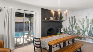 A dining area with a wooden table, chairs, a bench, a fireplace, and a cactus mural.