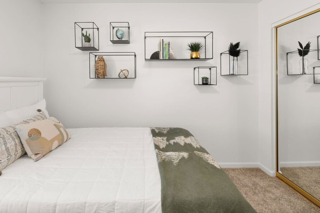 Une chambre à coucher comprenant un lit, des oreillers, une table de chevet, un miroir et des étagères murales décoratives.