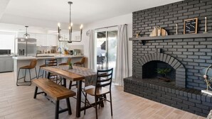 A modern kitchen with a central island, a dining area with wooden furniture, and a brick fireplace.