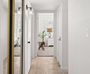 A hallway with a wooden floor, white walls, and a door leading to a room with a bed and a plant. - Westgate Wonder! With Pool, Putting Green, newly remodeled!  (Phoenix)