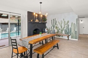 Un espace repas avec une table et des bancs en bois, une cheminée et une fresque murale représentant des cactus.