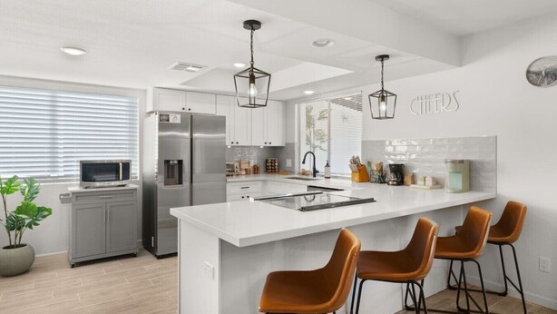 A modern kitchen with a large island, bar stools, stainless steel appliances, and pendant lighting.