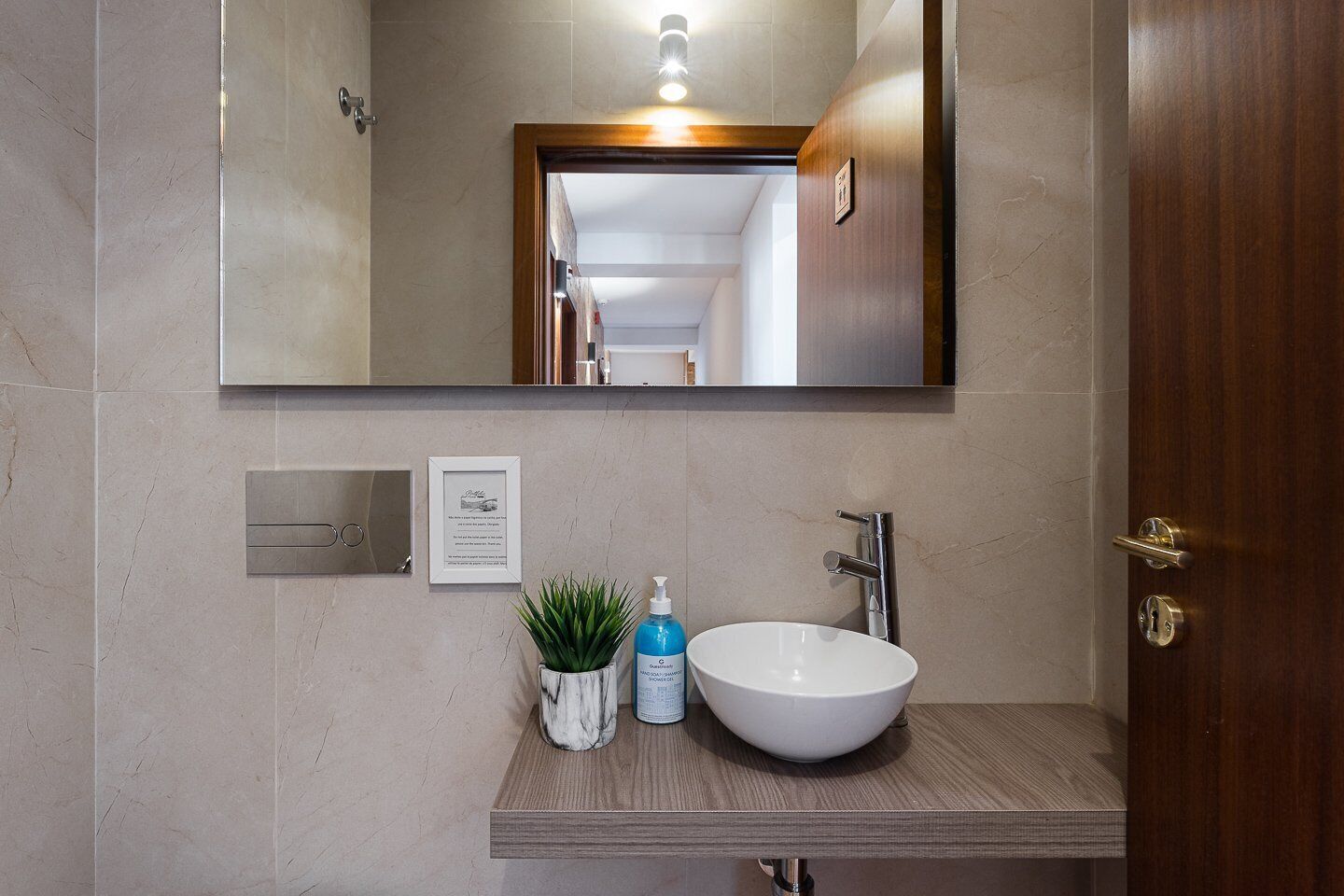Un baño moderno con un lavamanos de mármol, un espejo, un cuadro enmarcado y una planta en maceta.