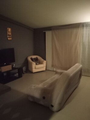 A room with a sofa, a chair, a TV, and a curtain.