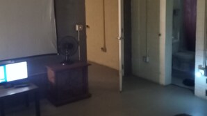 Une pièce comprenant un lit, un bureau, un ventilateur et une porte donnant sur une autre pièce.