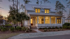 A two-story house with a porch, surrounded by trees and a gravel driveway.