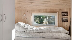 A bedroom with a bed, a window with a view of trees and a statue, wooden walls, and a white wardrobe. - Stunning home in Rødby with sauna (Rødby)