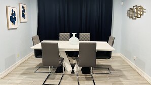 A dining area with a rectangular table, four chairs, a vase, and a dark curtain backdrop. - 3bdrm Entertainment Home (orlando)