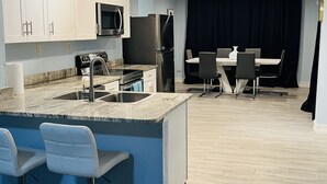 A modern kitchen with white cabinets, a built-in microwave, a stainless steel refrigerator, and a bar area with bar stools. - 3bdrm Entertainment Home (orlando)