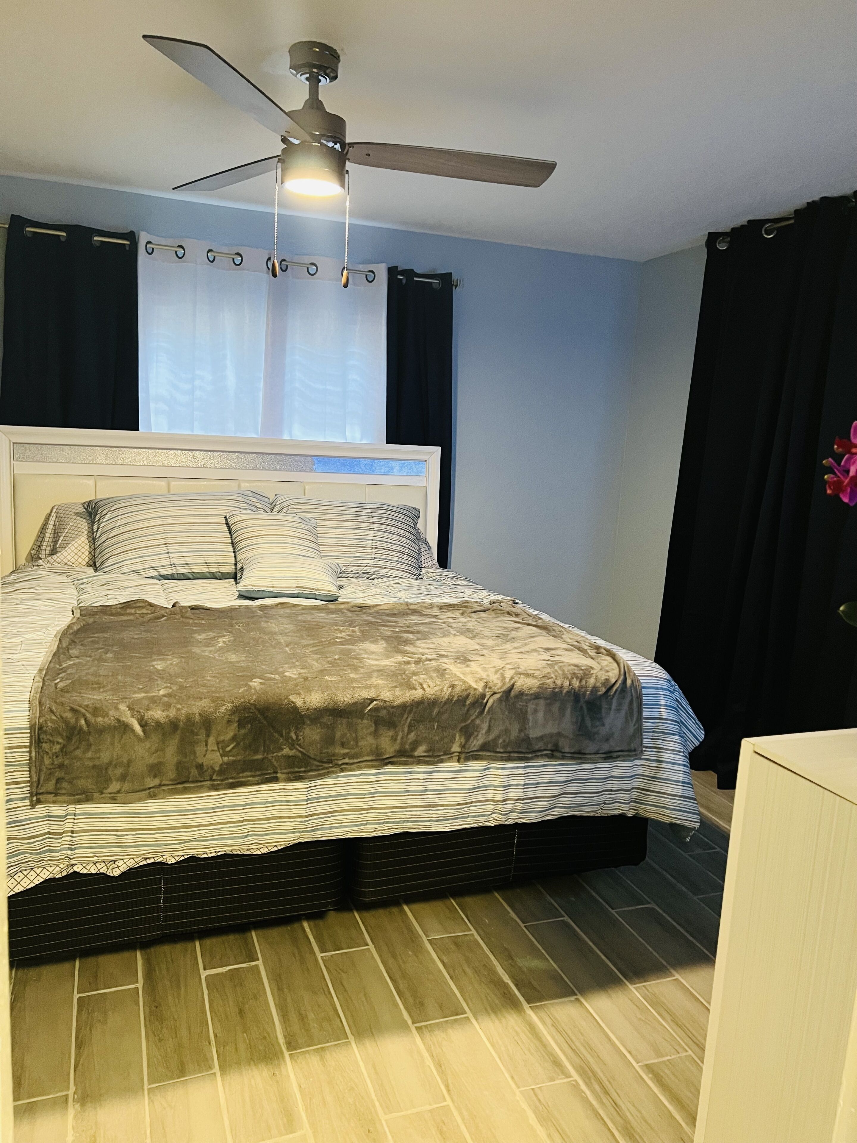 Une chambre à coucher avec un lit, un ventilateur de plafond et une fenêtre avec des rideaux.