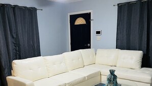 A living room with a white sectional sofa, a glass coffee table, a ceiling fan, and a door with a dark curtain. - 3bdrm Entertainment Home (orlando)