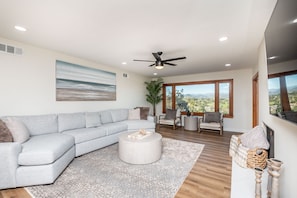 A modern living room with a grey sectional sofa, a round coffee table, and a large window offering a view of the landscape. - Amazing Escape with Game Room, Pool & Hot Tub (Escondido)