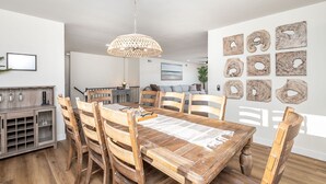A dining area with a wooden table and chairs, a hanging light fixture, and a wall with abstract art. - Amazing Escape with Game Room, Pool & Hot Tub (Escondido)