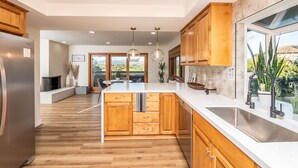 A modern kitchen with wooden cabinets, a stainless steel refrigerator, and a large island with a sink. - Amazing Escape with Game Room, Pool & Hot Tub (Escondido)