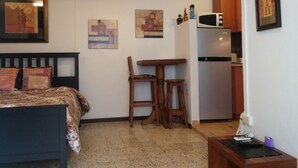 Ein kompaktes Zimmer mit einem Bett, einer kleinen Essecke mit Stühlen, einer Mikrowelle und einem Kühlschrank.