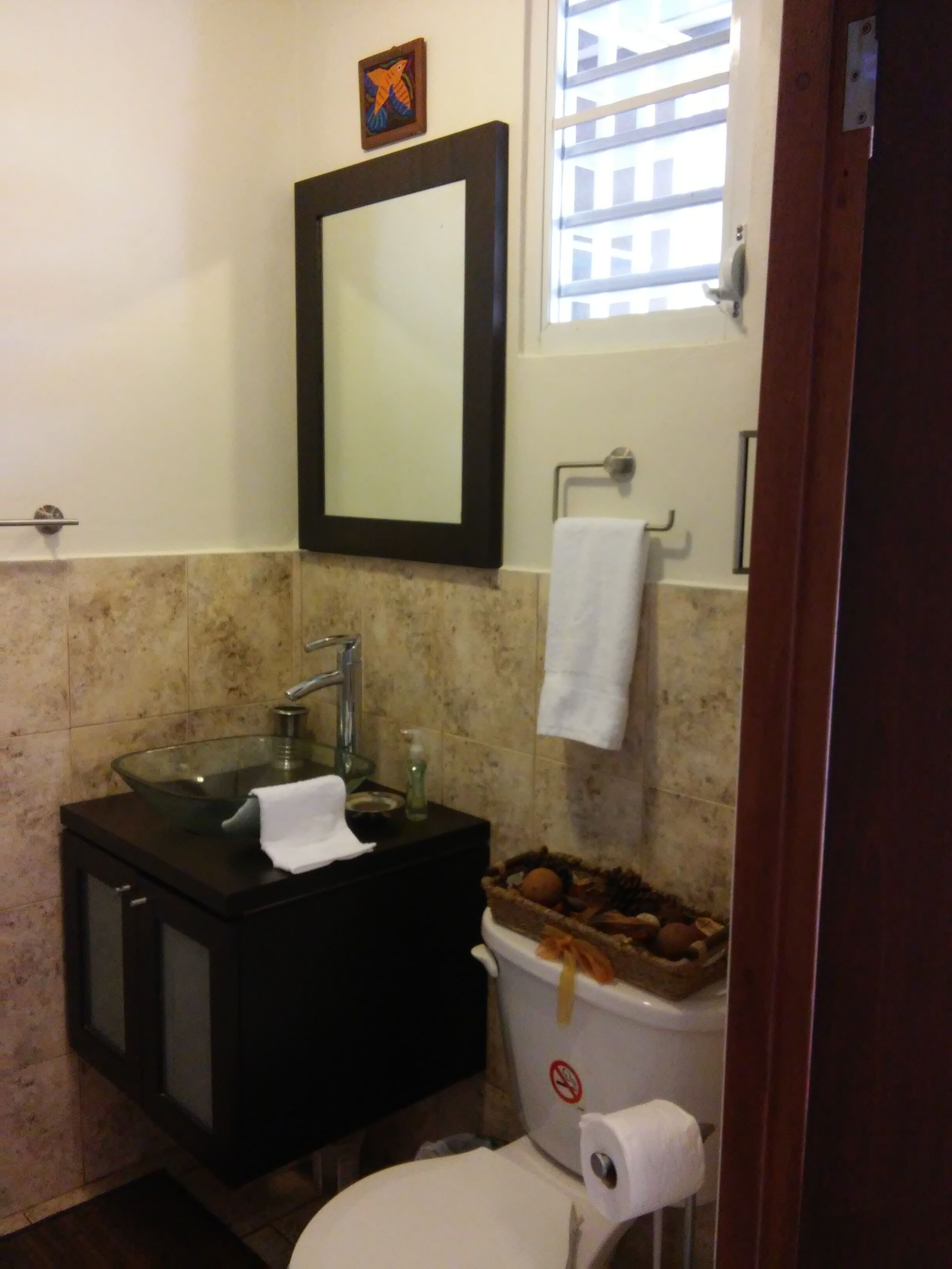 A bathroom with a glass sink, a mirror, a toilet, and a trash bin.