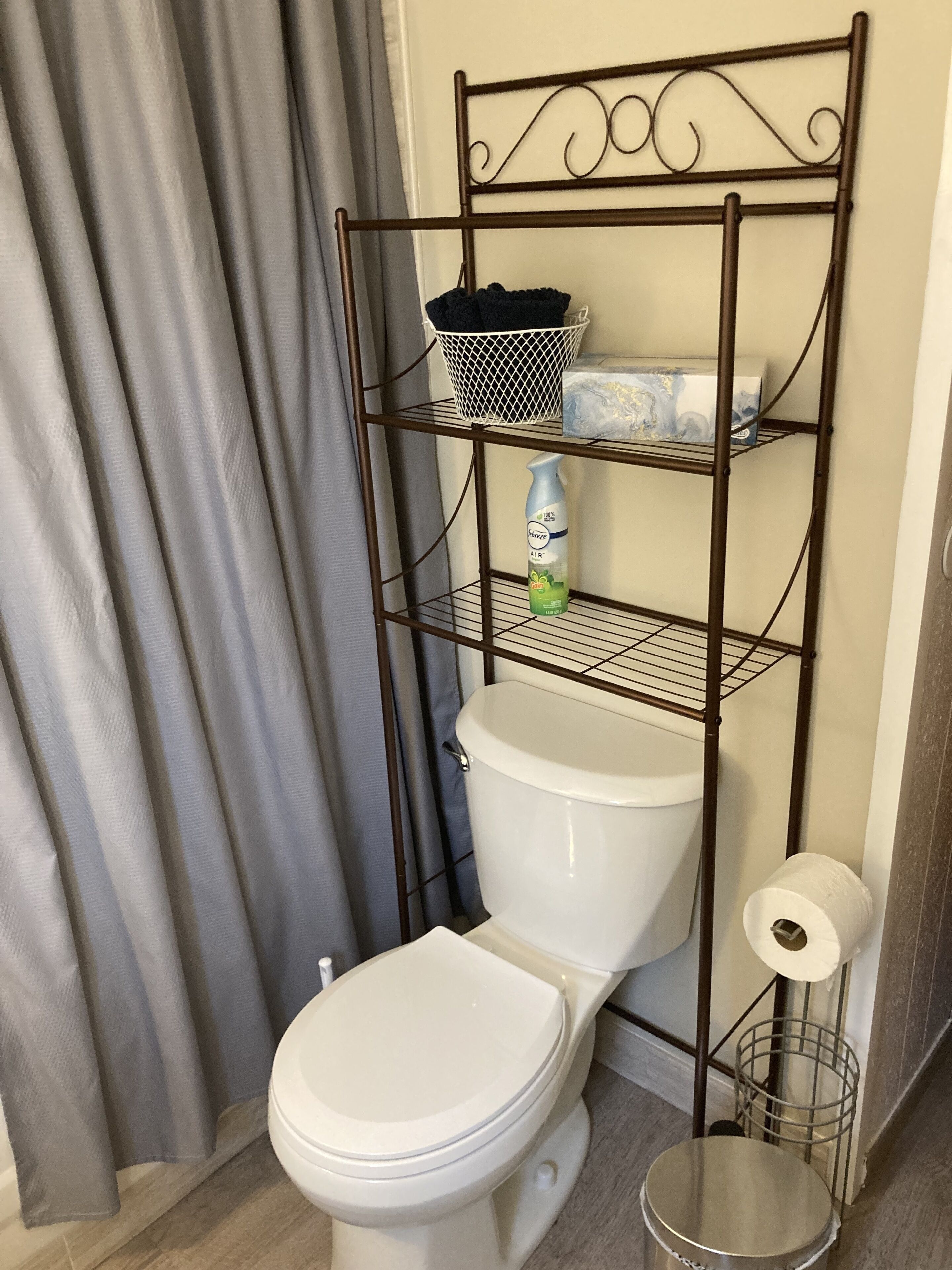 Ein Badezimmer mit einer weißen Toilette, einem Metallregal mit einem Korb und einer Flasche sowie einem Toilettenpapierhalter.