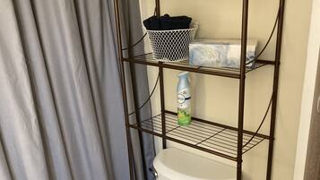 Ein Badezimmer mit einer weißen Toilette, einem Metallregal mit einem Korb und einer Flasche sowie einem Toilettenpapierhalter.