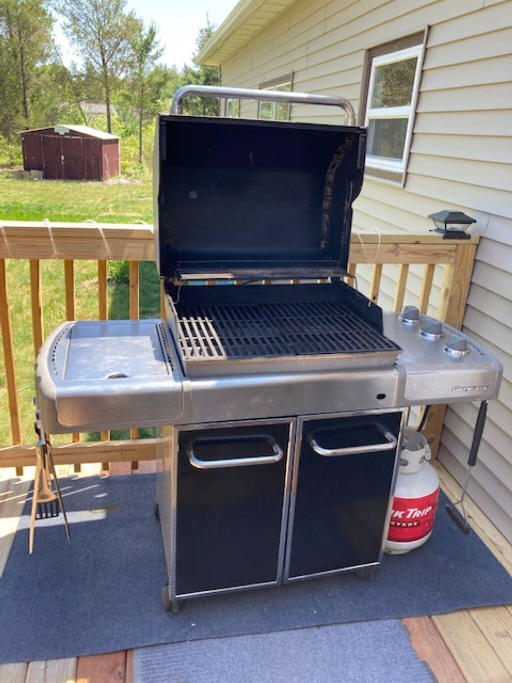 Una parrilla portátil con un quemador lateral y un tanque de propano.