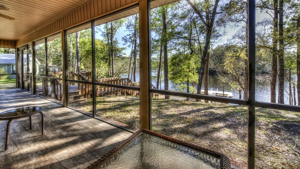 A covered outdoor area with large windows, a wooden ceiling, and a view of a forest and lake. - Osprey House, Osprey House (Wakulla County)