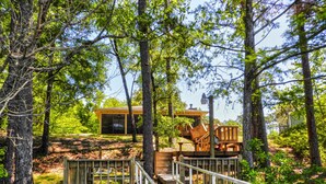 A wooden cabin with a deck and stairs leading to a covered area, surrounded by trees. - Osprey House, Osprey House (Wakulla County)