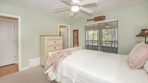 A bedroom with a bed, a ceiling fan, a dresser, a window with blinds, and a door. - Osprey House, Osprey House (Wakulla County)