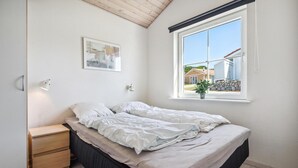 Un dormitorio con una cama individual, una mesita de noche, una ventana con vistas a casas y un cuadro en la pared.