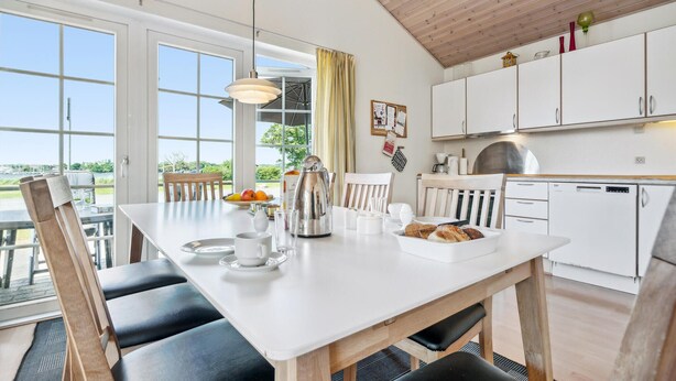 Una cocina moderna con armarios blancos, una mesa de comedor con sillas y vistas al exterior.