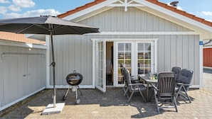Un patio techado con una parrilla, mobiliario exterior y una puerta que da a un espacio interior.
