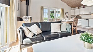 Una sala de estar moderna con un sofá de cuero negro, una mesa blanca y una zona de cocina con armarios blancos.