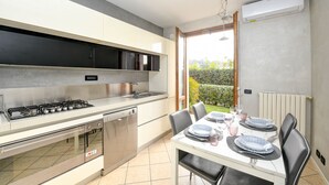 A modern kitchen with a gas stove, dishwasher, and a dining area with a table set for four. - Maison Elisa a Manerba By Bookinggardalake (Manerba del Garda)