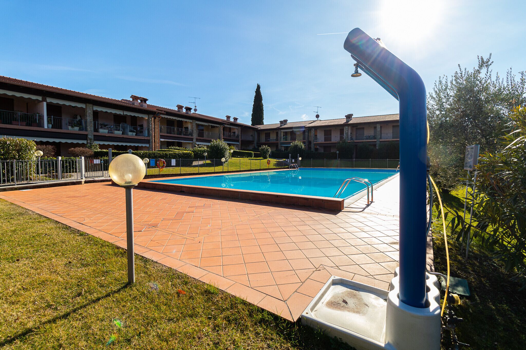 A swimming pool with a blue water slide, surrounded by a tiled patio and a building with balconies.