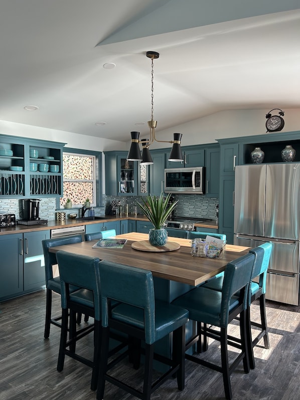 A modern kitchen with teal cabinetry, a wooden island, and black chairs.