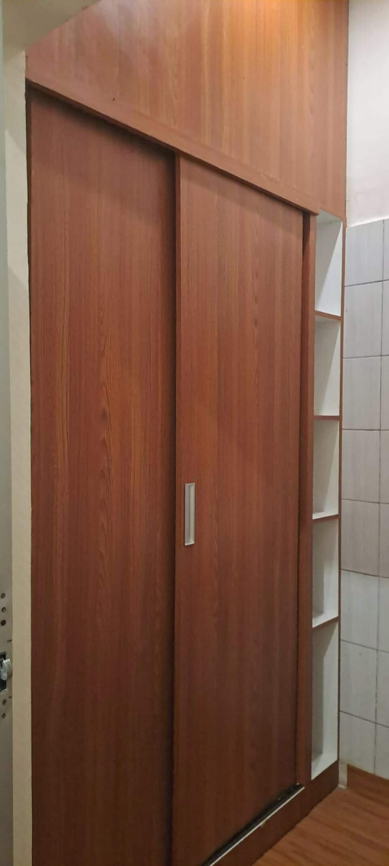 Un armario de madera con puerta corredera y un estante pequeño.