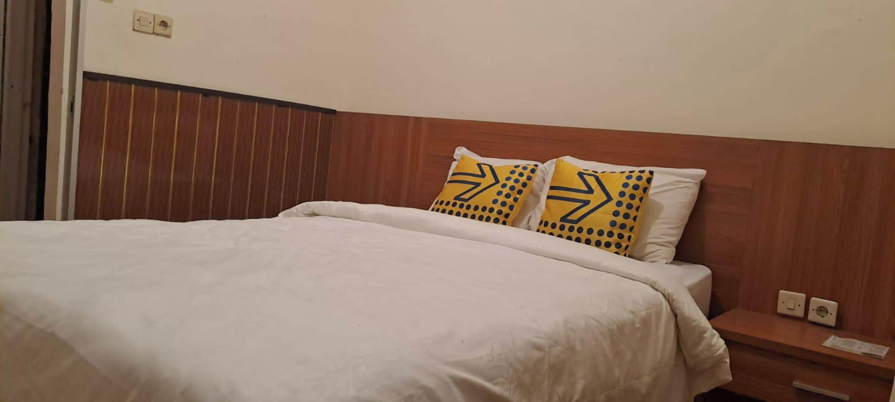 A bed with white bedding and two pillows with yellow and black patterns.