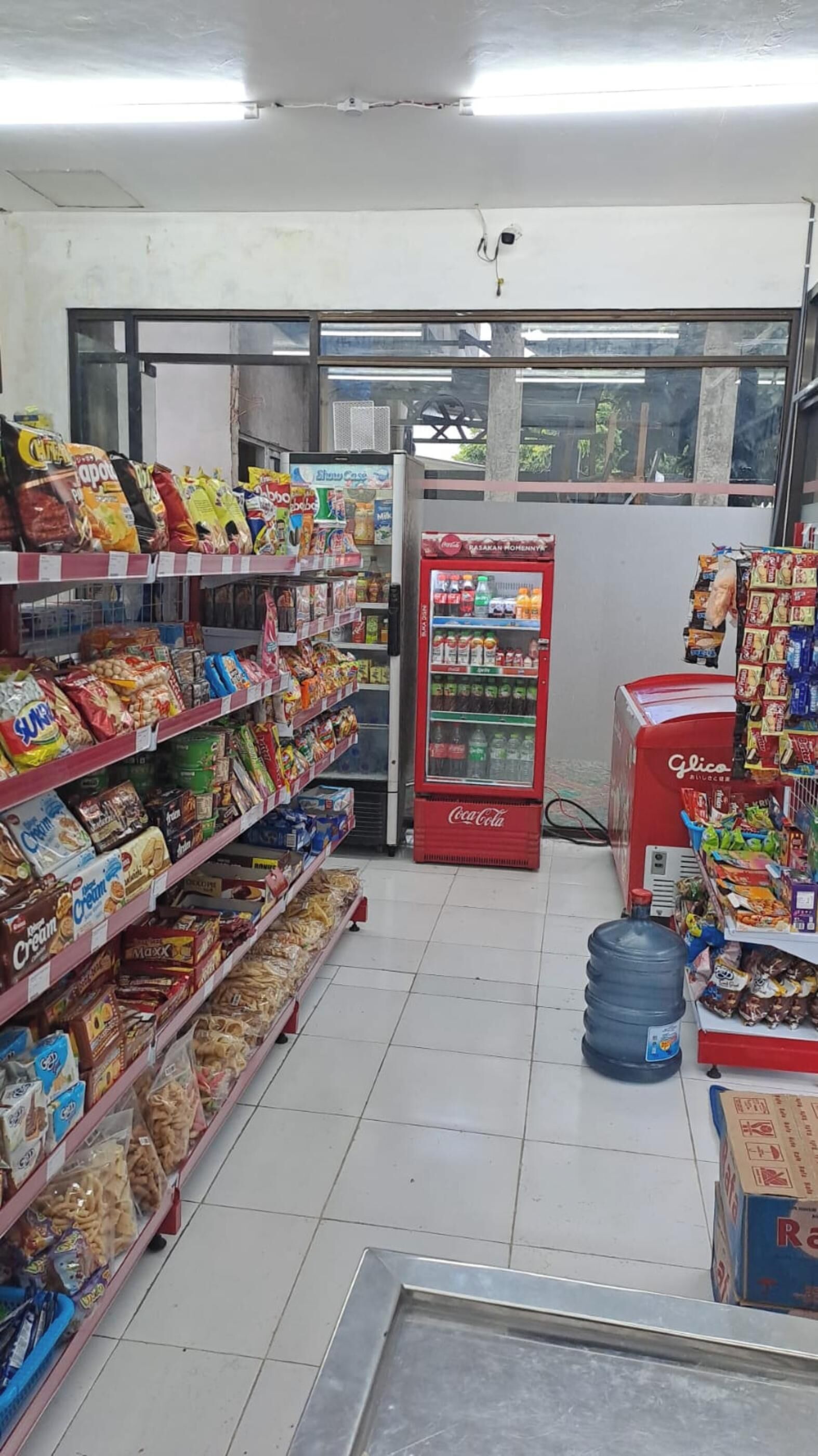 A grocery store with shelves stocked with snacks, a Coca-Cola refrigerator, and a water dispenser.