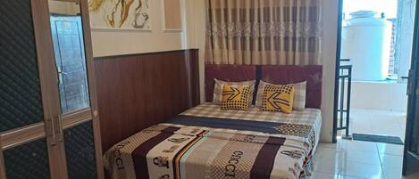 A hotel room with a bed, curtains, a window, and a door.