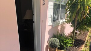A building entrance with a number '43' on the wall, a door, a small rug, and two potted plants.