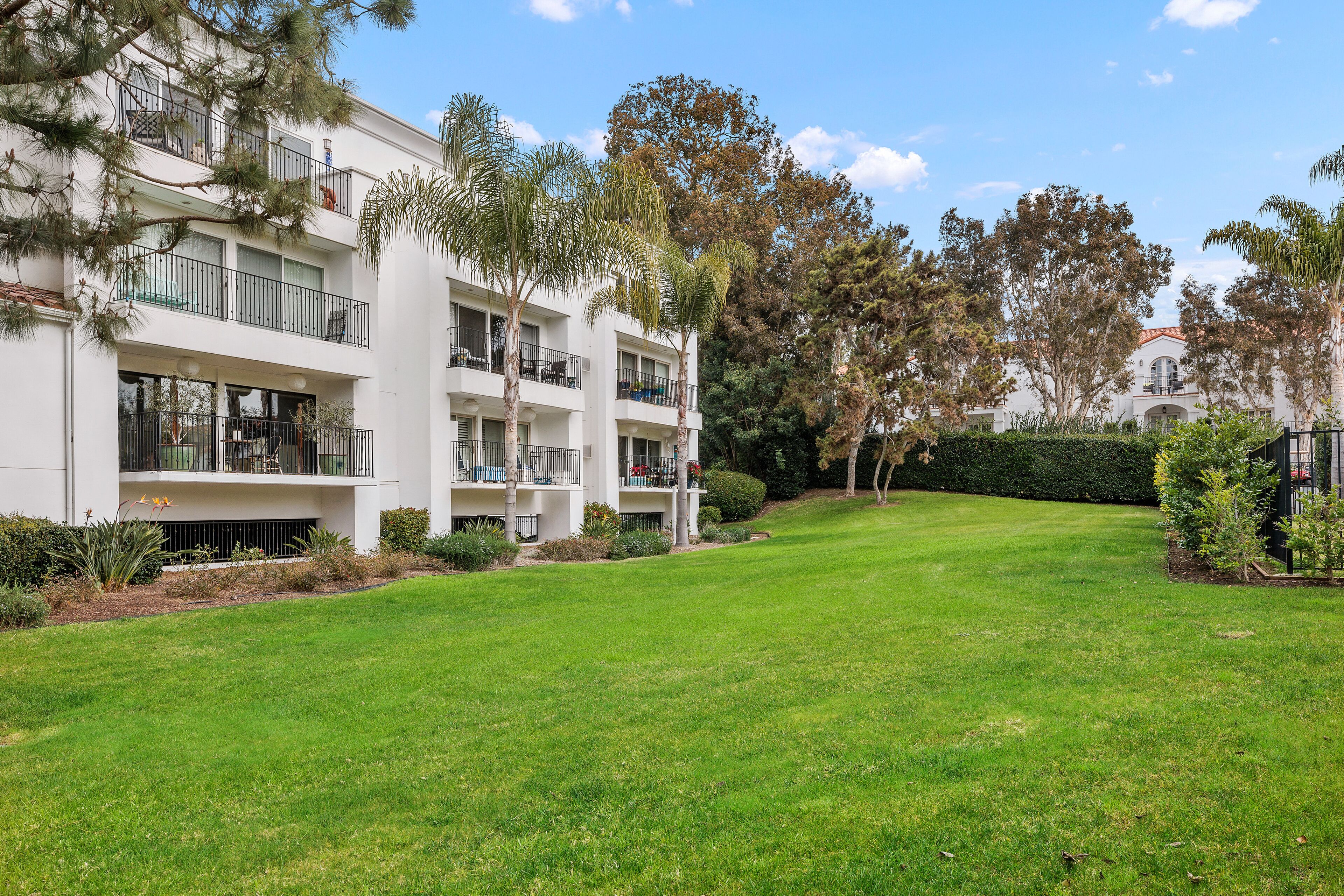A multi-story building with balconies, surrounded by a well-maintained lawn and various trees.