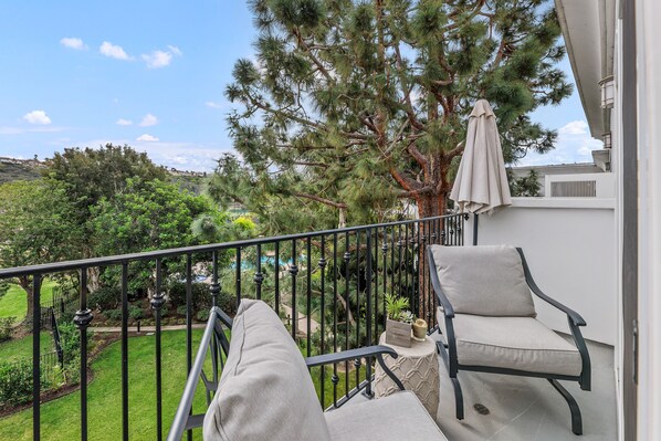 Ein Balkon mit Blick auf einen Pool und Bäume, ein Stuhl und ein kleiner Tisch mit einer Pflanze.